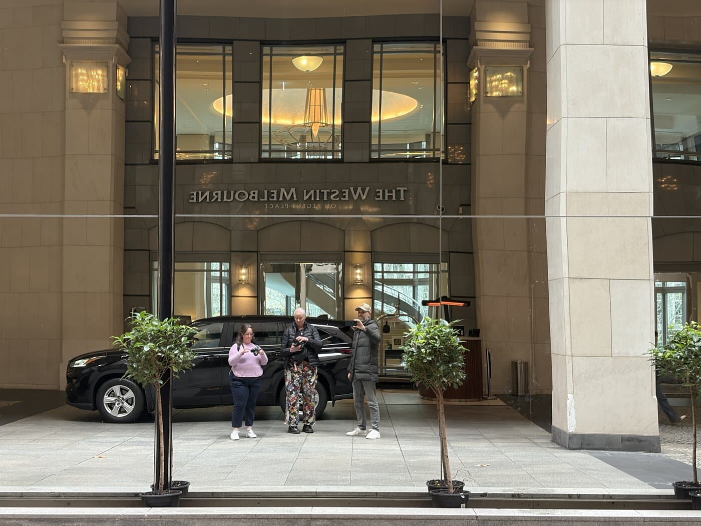 Daniel Bilsborough with students Megan and Sage reflected in the mirrored glass facade of The Westin Melbourne during a photography course