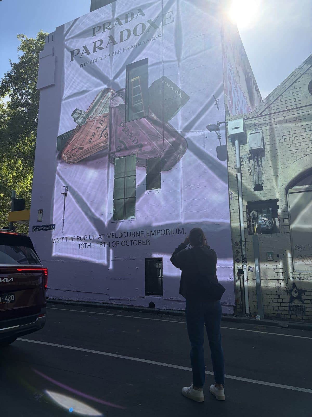 Eliza photographing a large painted wall advertisement with the sun directly behind the building in Melbourne CBD