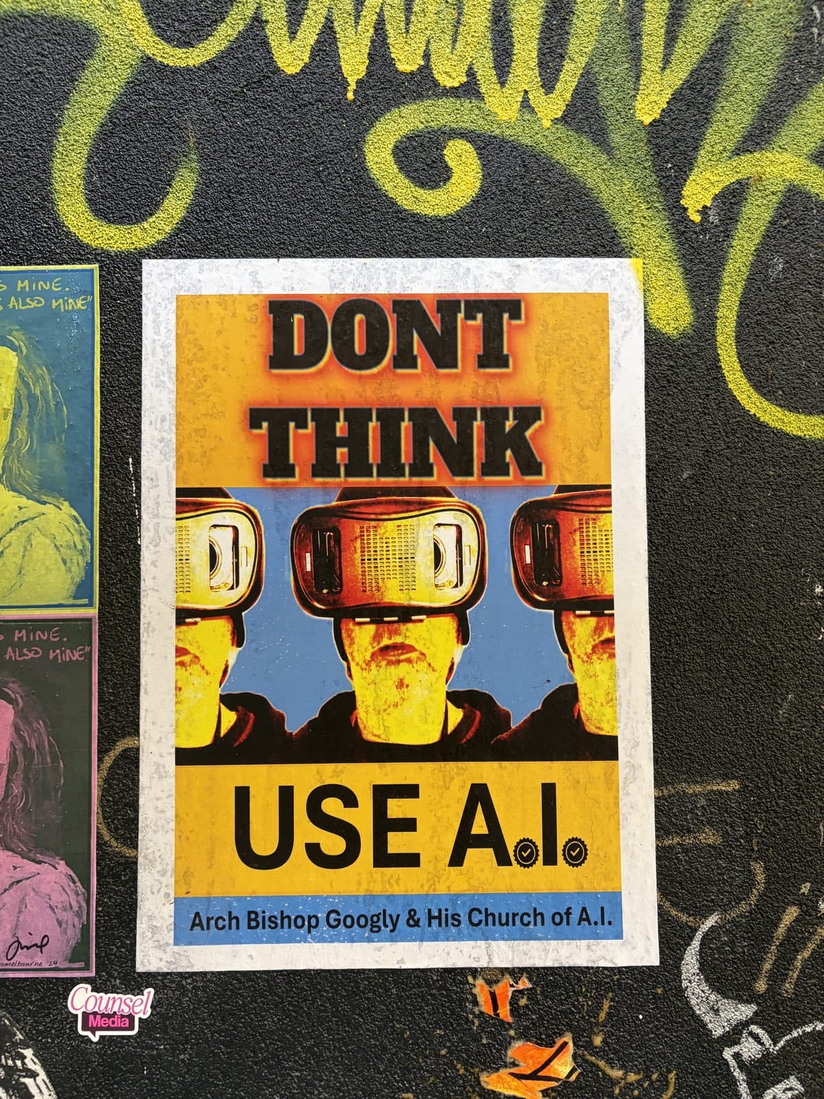 Paste-up poster on a black graffiti wall in Melbourne reading Don't Think Use A.I. with three figures wearing virtual reality headsets
