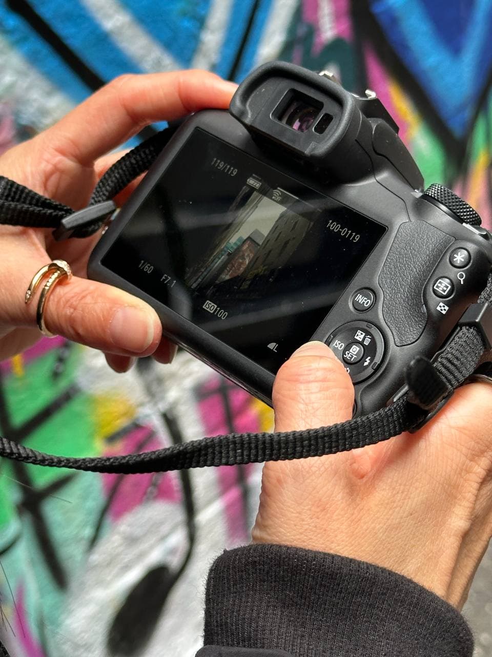 Canon R100 LCD screen showing manual mode settings: 1/60s, f/7.1, ISO 100 with street art in the background during a Melbourne photography course
