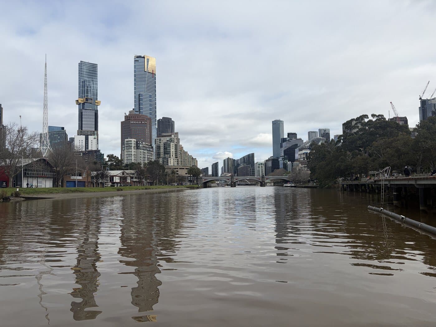 Melbourne city skyline and the Arts Centre spire seen low across the Yarra River with reflections in the water