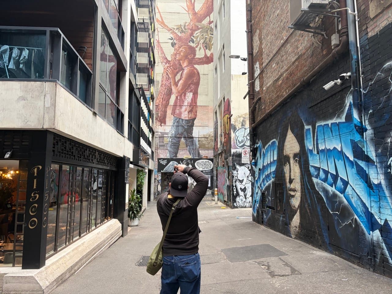 Ron shooting with his Sony A7CR in a Melbourne laneway with street art murals on both walls during a photography course