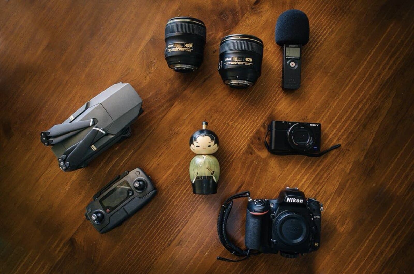 A flat-lay of Daniel Bilsborough's camera gear: a Nikon D750, two prime lenses, a Sony RX100, a Zoom recorder, and a DJI drone on a wooden table
